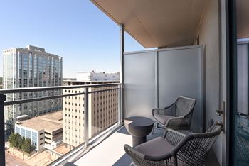 A balcony with two chairs and a table overlooks a cityscape.